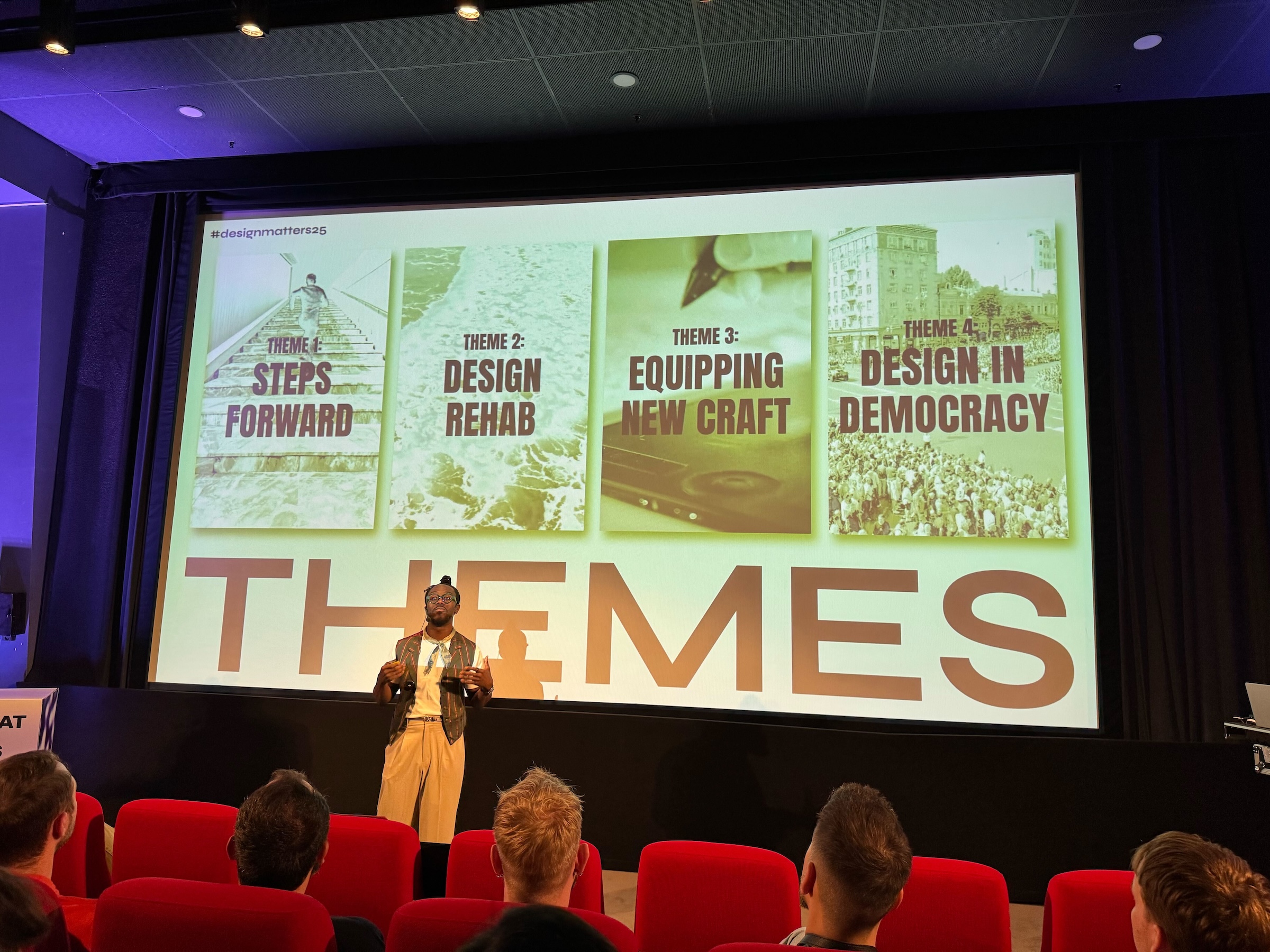 テーマがスクリーンに写っている。「Steps Forward」「Design Rehab」「Equipping New Craft」「Design in Democracy」と書かれている。