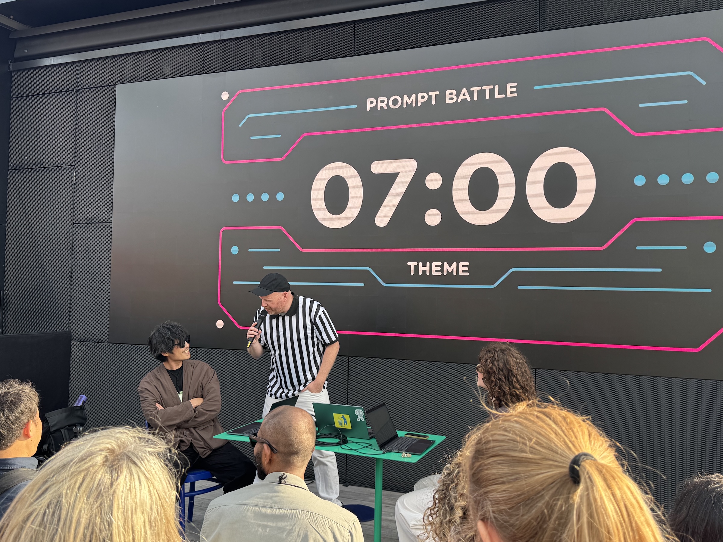 7:00と書かれたタイマーとPrompt battleと書かれたスライドの後ろに、審判と挑戦者が3名。